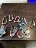Nine assorted carabiner clips of varying types and two pulley systems displayed on a dark surface.