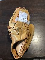 Top angle view of the light brown rawhide leather baseball glove showing the fingers and inside palm area with a white tag labeled 115.
