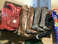 Seven pairs of boots laid out: variations in color including red, brown, gray, and black. Black Skechers boots are included.