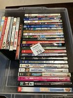 Top view of 31 assorted DVDs in a transparent plastic container showing mostly spines and titles of individual DVDs, all stacked horizontally.