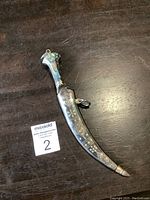 Full view of the Jambiya Arabian curved dagger with mother of pearl handle and decorated sheath on a wooden surface.
