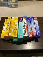 Photo showing six rolls of yellow paper grease pads (wax paper) on the left and several rolls of cling wrap and aluminum foil in boxes on the right.