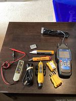 Full view of all included items on wooden surface showing various electrical and automotive testing tools, cables and adapters.