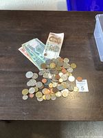 Photo of mixed coins and currency on a wooden surface with a lot number card visible.