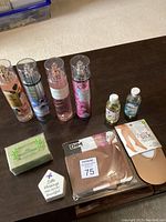 Full lot display of 4 fragrance mists, 2 oils, olive oil soap bar, and 2 hosiery items on dark table.