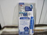 Full front view of the unopened Vital Health electric toothbrush package showing the toothbrush handle, multiple brush heads, interdental tools, and product information on packaging.