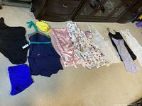 Photo showing 9 assorted women's nightwear and bath suits/cover items laid on floor including swimsuits (black, navy with yellow/turquoise), silky robe, floral and sheer covers, lace slips.