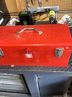 Closed red metal toolbox on a workbench.