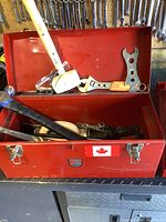Front open view of red metal toolbox with various tools including hammer, mallet, adjustable wrench, double open-end wrench inside