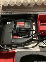 Open case showing black and gray Skil jig saw with power cord coiled inside and red compartments for blades.