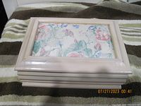 Small light-colored wooden jewelry box with a glass top showing floral fabric beneath, placed on a textured blanket.