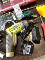Photo showing Ryobi 4 Volt cordless drill, charger, power adapter, green extension cord, yellow plastic scraper, and safety goggles.
