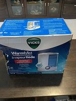 Photo of the front side of the Vicks Warm Mist Humidifier box showing product image, brand logo, and features.
