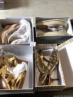 Eight pairs of women’s shoes in boxes and arranged on floor showing various styles and colors including wedges, sandals, heels, and flats.