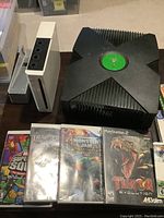 Xbox original and Nintendo Wii consoles shown with multiple game cases including Turok Evolution, Monster Jam, and Transformers.