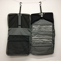 Interior view of garment bag showing hanging hooks, multiple zippered sections including mesh and clear pockets, internal straps, and areas for clothing organization