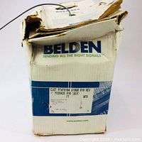 Damaged white cardboard box of Belden coaxial cable with product label showing specifications and length.