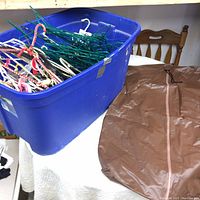 Blue bin filled with assorted used hangers of different types and colors beside a brown garment bag on a table.