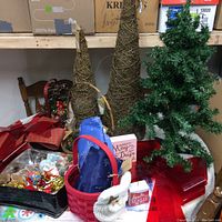 Photo showing two cone-shaped natural fiber trees, artificial 3-foot green Christmas tree, red basket with ribbons, assorted ornaments and plaques.