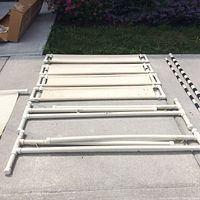 Foldable white plastic tubular frame parts and fabric panels for dog jump training laid out on concrete.
