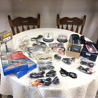 Wide table view showing entire electronics collection including Dymo label maker, phone sanitizer, numerous cables, blank CDs/DVDs, and car shaver.