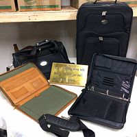 Photo showing the American Tourister black carry-on suitcase, leather portfolio, executive binder, and motivational plaque placed together on a surface.