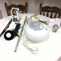 Wide view showing all lot items on table: vaporizer, propeller, lamp, door handle, wiper blade, and tealight holders in box.