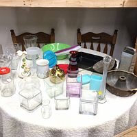 Wide view showing a variety of household items including glass vases, cake pans, plastic and ceramic bowls, grater, and other kitchenware on a table.