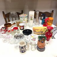 Overview of all items on table including glassware, ceramics, mugs, decorative vase, thermos, and storage containers.