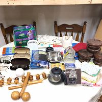 Wide view photo showing all household items arranged on a table including massagers, glasses, coffee pot, bowls, diapers, and textiles.