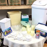 Full view of all items including bowls, candles, coolers, garbage cans, puzzle, and glass bowl on table with packing boxes in background.