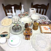 Overview of assorted household items on table with two wooden chairs behind