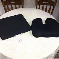Two black medical cushions displayed on a round table, one rectangular and one contoured with a U-shaped cutout.