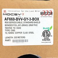 Label on box showing Mocsy 7 RG6 cable specifications: AF660-BVV-GY-3-BOX, standard shield, bonded foil, 60% braid, gray PVC, tested to 3GHz, 18AWG copper clad steel conductor, length 305 meters.