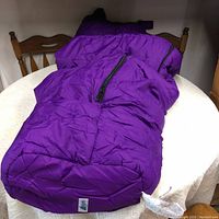 Purple winter sleeping bag displayed on a table, showing size and shape.