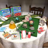 Photo of garden items including two boxed Topsy Turvy Tomato Planters, ceramic frog, turtle figurines, cherub statues, small planter pot, artificial grass mat, flower-shaped holders, and various tags.