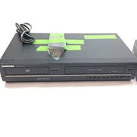 Samsung DVD/VCR combo unit with power cord on top and green tape labels