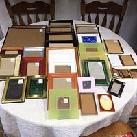 Photo showing an assortment of 31 picture frames laid out on a white tablecloth with varying sizes, colors, and styles including gold, black, wood, green, pink, red, and orange frames.