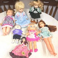 Full view of six retro dolls on table showing variety in hairstyle, dress, and face paint.
