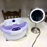 Foot massager and lighted mirror placed on a table with a wooden chair in the background