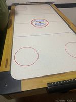 Full view of air hockey table from one end showing playing surface, scoring system, and brand logo.