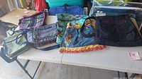 Overall view of the six bags on a table including messenger bags, backpack, and sling pack