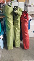 Three folded chair bags standing upright: two light green, one red, each with carrying straps.
