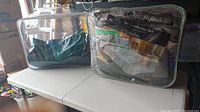 Two bedding and mattress items in plastic and clear storage bags, sitting on folding table.