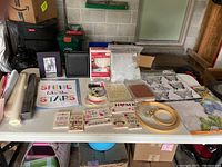 Overview photo showing various craft supplies spread on a table including signs, fabric, embroidery hoops, and containers with beads and bells.