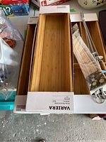 Two Ikea VARIERA bamboo cutlery trays, one inside packaging, shown on a concrete surface and table.