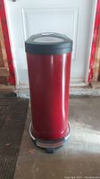 Front view of tall red metal garbage can with black base and lid, showing step-on pedal at the bottom.