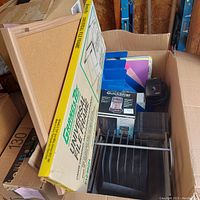 Photo showing the universal file frame box, bulletin board, magazine holders, tape dispenser, file sorter, and electric pencil sharpener inside a large cardboard box.