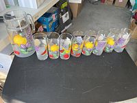 Full set view of pitcher and eight glasses, showing fruit-themed decals on each item