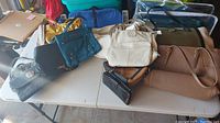Group of ten purses and one wallet laid out on a folding table in various colors and styles.